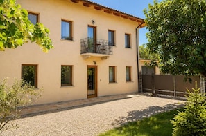 A two-story building with a balcony on the upper floor, a gravel driveway, and a wooden fence.