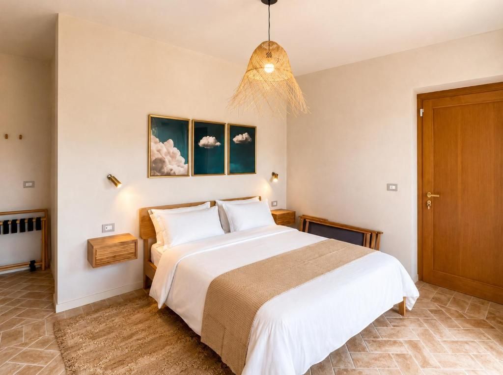 A bedroom with a bed, bedside tables, a wall-mounted artwork, a door, and a hanging light fixture.