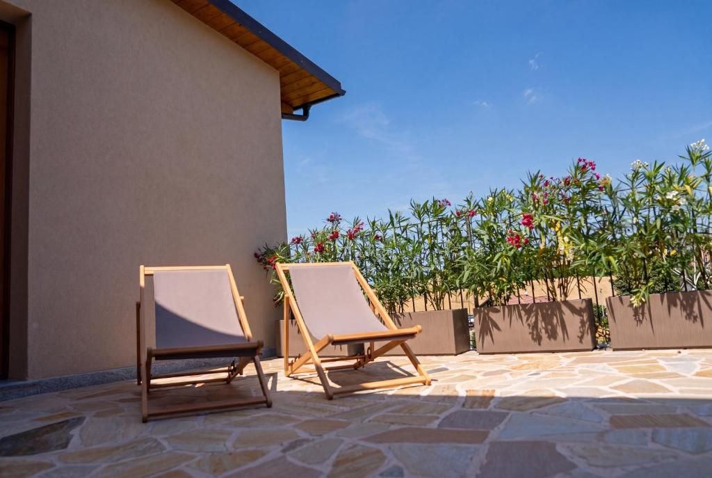 Two wooden lounge chairs with canvas seats on a stone patio, adjacent to a building with a beige facade and a wooden roof.