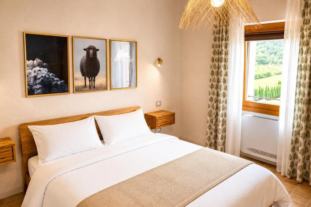 Une chambre d’hôtel avec un grand lit, deux tables de chevet, une lampe fixée au mur et une fenêtre avec des rideaux.