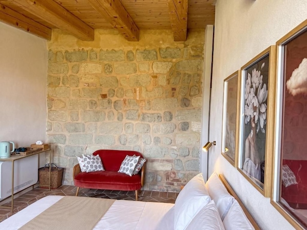 A room with a stone wall, a red sofa, a bed, and a painting.