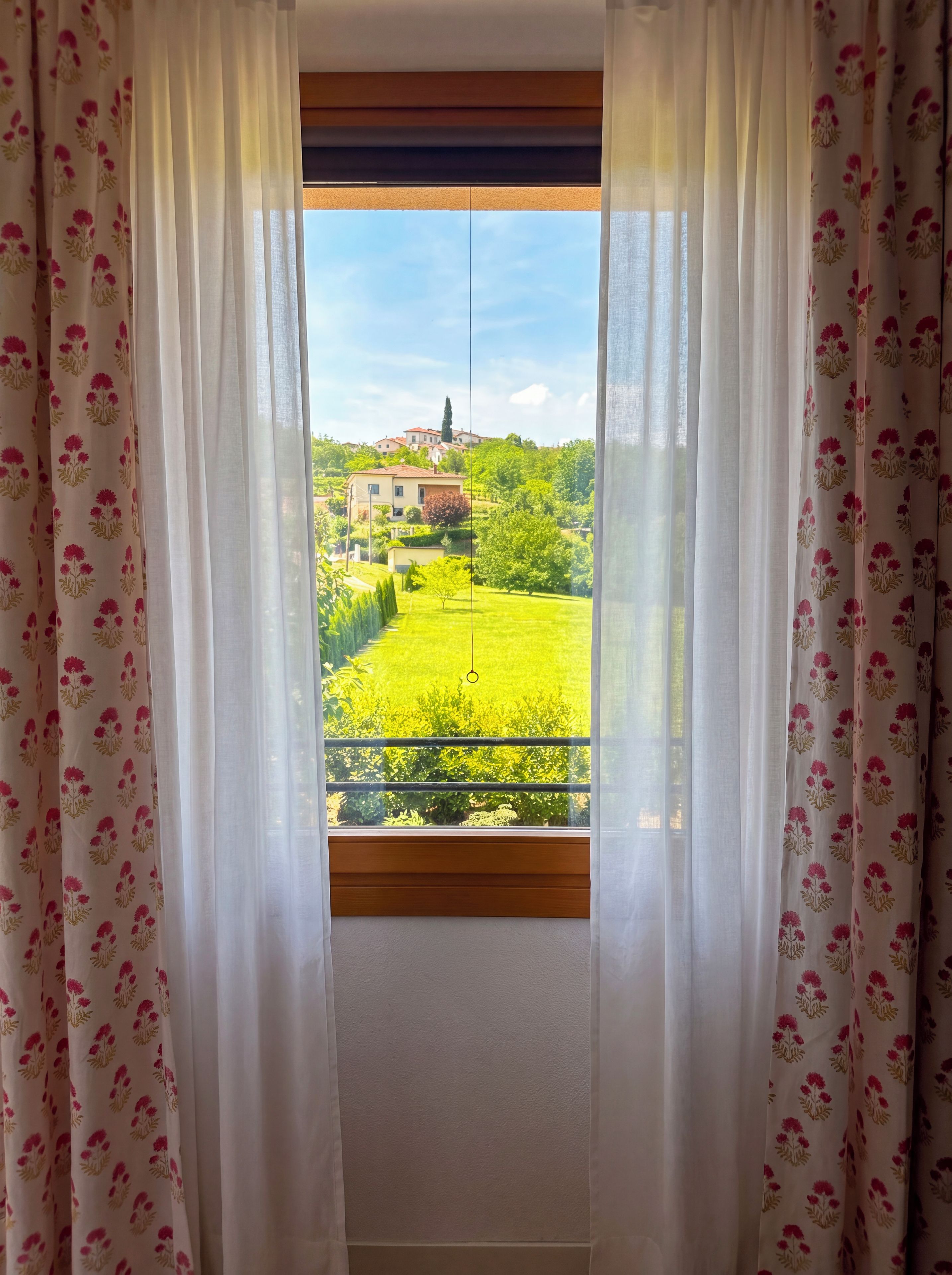 Ein Fenster mit Blick auf eine grüne Landschaft und Gebäude.