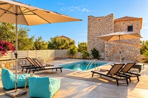 A poolside area with lounge chairs, a stone building, and a clear sky. - Villa Lydia, Luxury Stone Retreat with Private Pool (Agios Nikolaos)