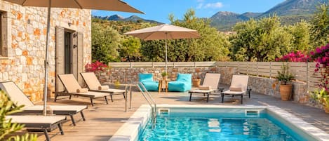 A poolside area with lounge chairs, umbrellas, and a stone building.