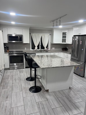 A modern kitchen with white cabinets, stainless steel appliances, a granite countertop, and a bar stool. - Charming Waterville Home on Quiet Street. Fully Furnished (Waterville)