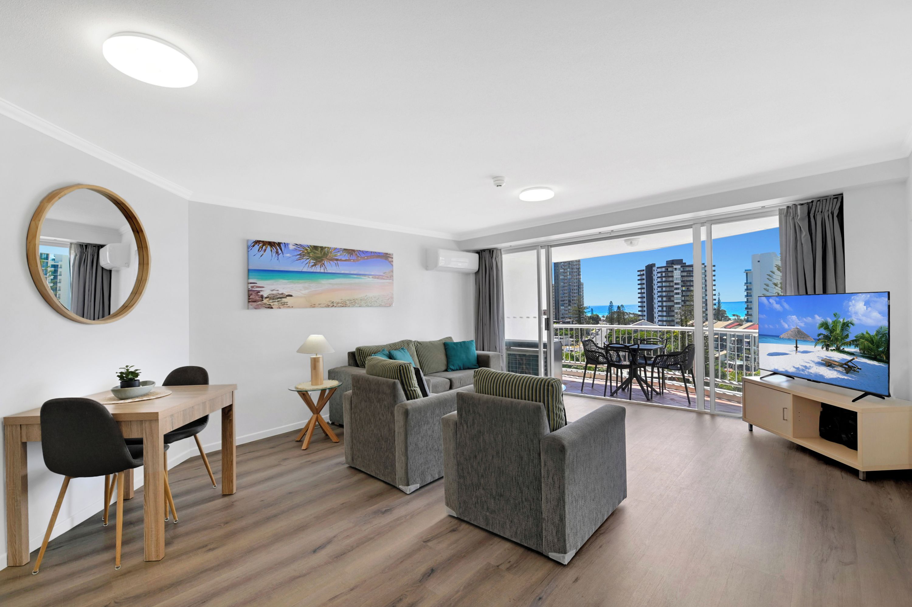 A modern living room with a dining area, a large window with a view of the city, and a flat-screen TV.