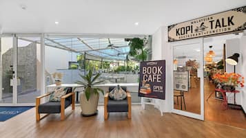 Un interior moderno con entrada por puerta de vidrio, un cartel para una cafetería de libros y un restaurante llamado 'KOPITALK'.