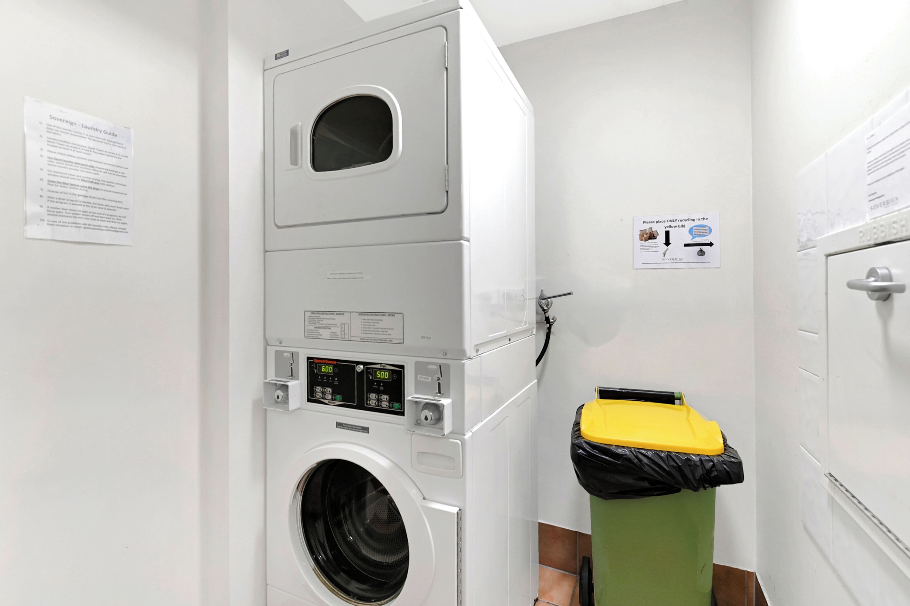 A laundry room with stacked washing machines, a dryer, and a recycling bin.