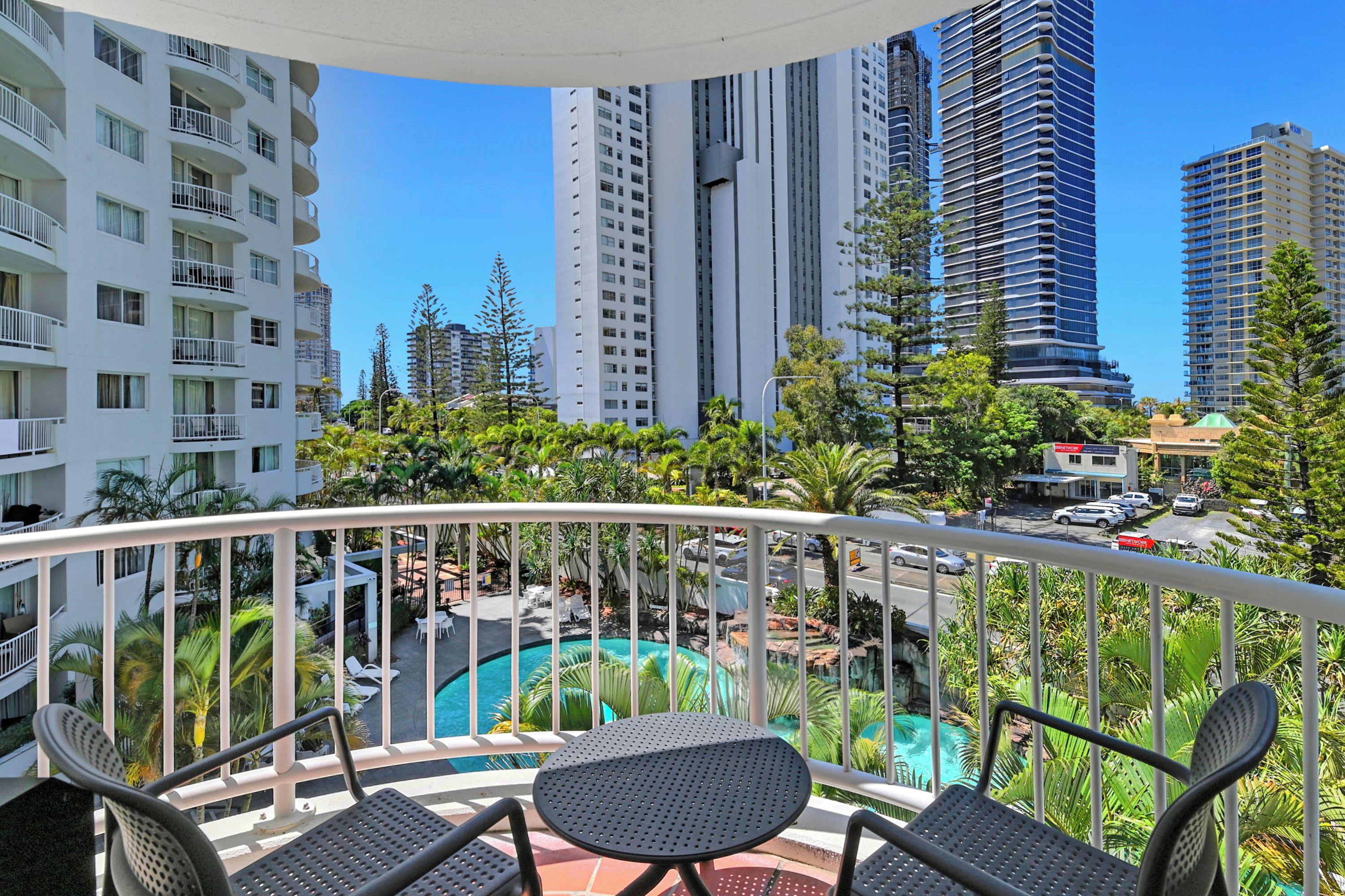A balcony with a pool, surrounded by tall buildings and greenery.