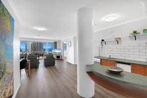 A modern living room with a flat-screen TV, a dining area with a table and chairs, and a kitchen with a sink and cabinets. - Deluxe Views At Sovereign (Surfers Paradise)