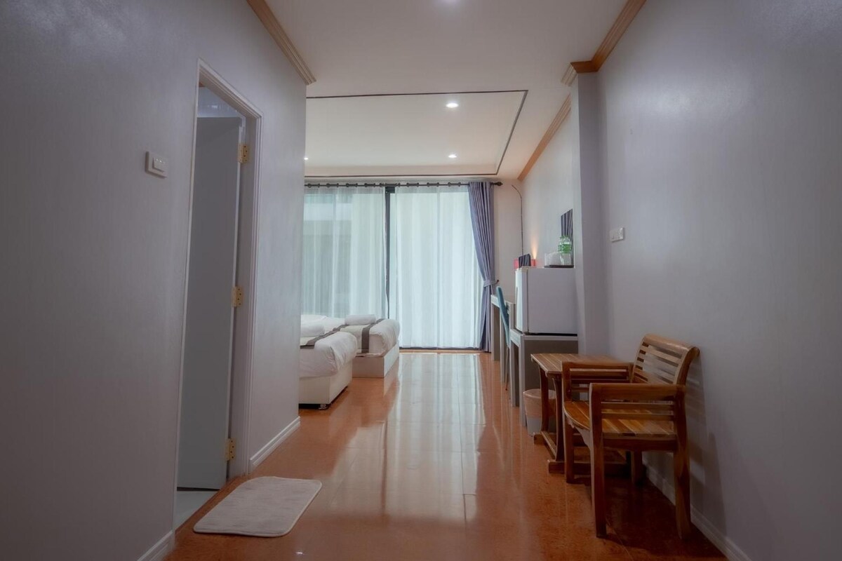 Un pasillo con una cama, una mesa de comedor con sillas y un refrigerador.