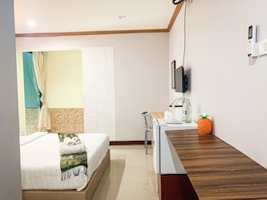 Une chambre d’hôtel avec un lit, un bureau, une chaise, un téléviseur fixé au mur et une petite décoration en forme d’ananas posée sur le bureau.