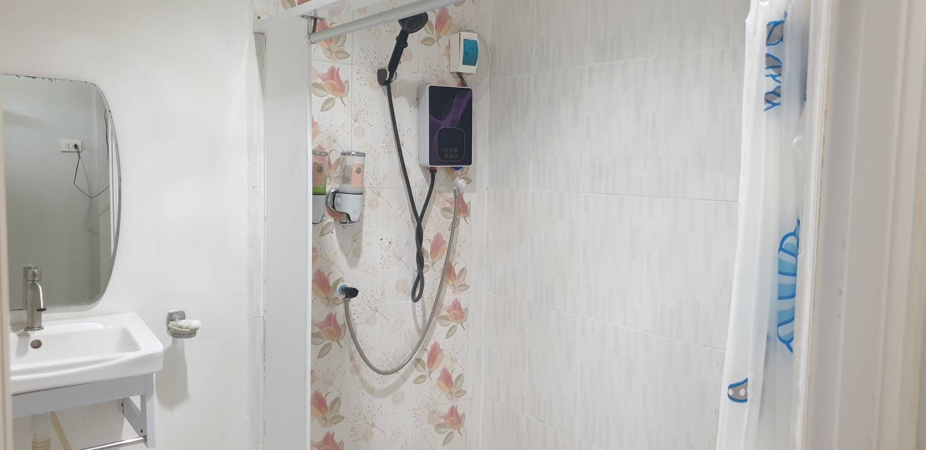 Une salle de bain avec un lavabo blanc, un miroir, une douche avec un rideau de douche à motifs floraux et un pommeau de douche à main.