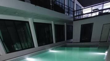 A swimming pool with a clear water surface, surrounded by a white pool deck and a glass barrier.
