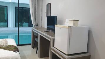 A hotel room with a bed, a desk with a computer, a refrigerator, and a window with a view of a pool.