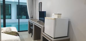 Habitación de hotel con cama, escritorio con computadora, refrigerador y ventana con vista a una piscina.