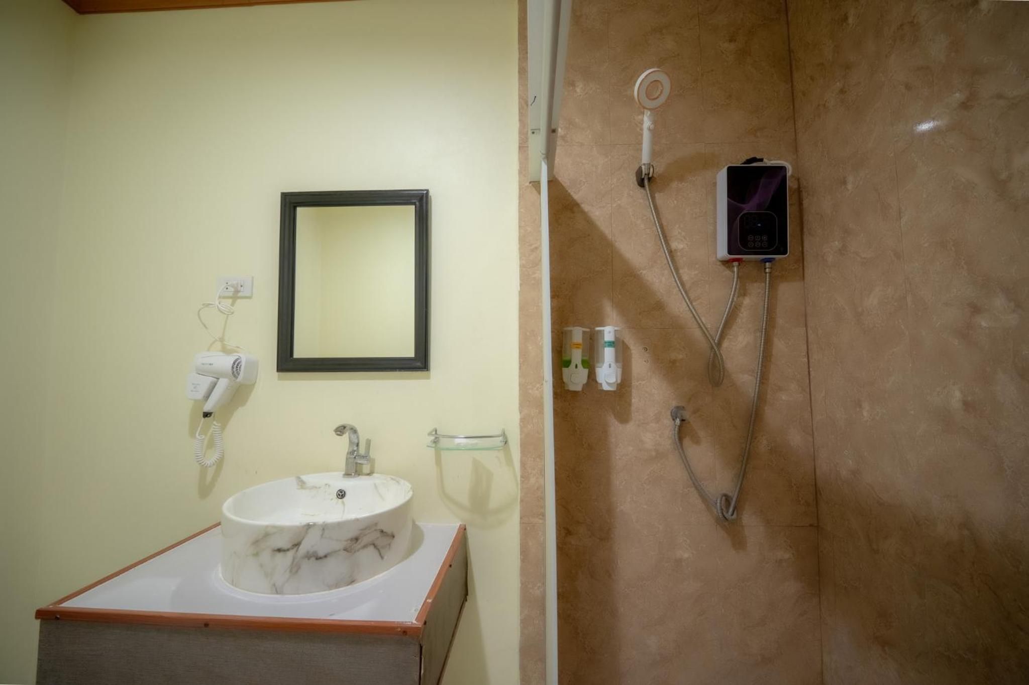 Un baño con lavamanos de mármol, un espejo, cabezal de ducha de mano y secador de mano.