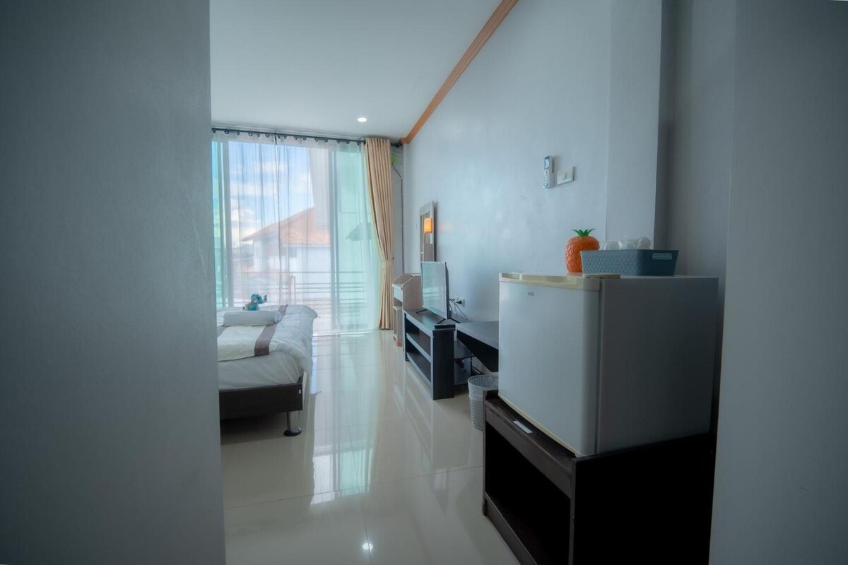 Una habitación de hotel moderna con cama, televisión, refrigerador y ventana con cortinas.