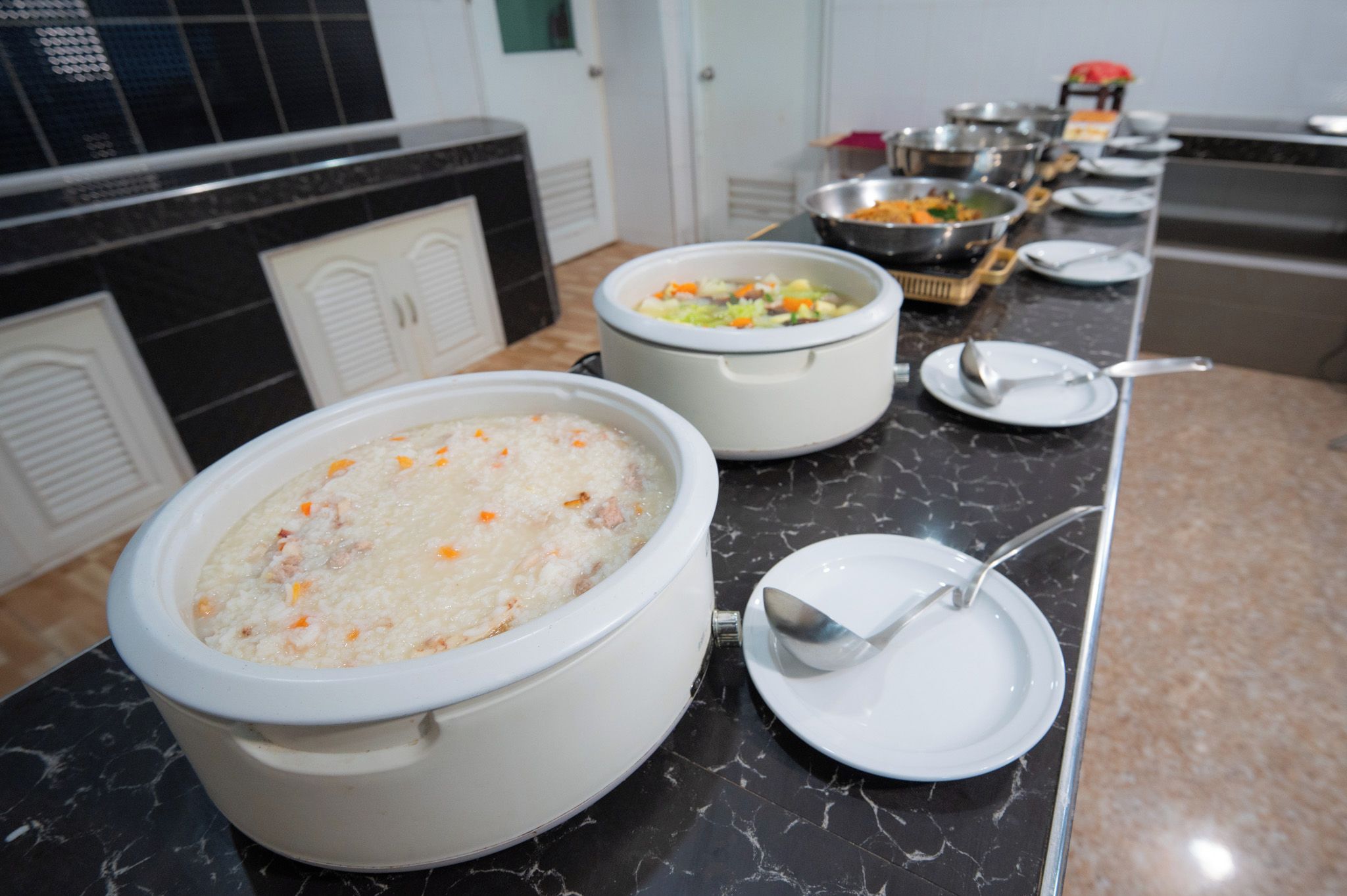 A buffet setup with large pots of food, serving utensils, and a marble countertop.
