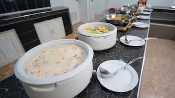 A buffet setup with large pots of food, serving utensils, and a marble countertop.