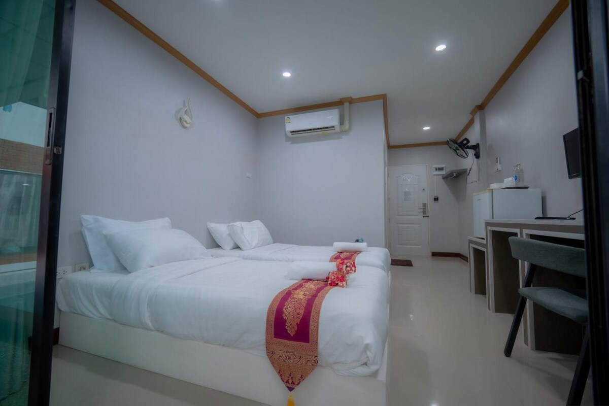 Habitación de hotel con dos camas, un escritorio, una silla, un equipo de aire acondicionado y un televisor.