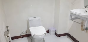 Un baño pequeño con inodoro, lavamanos y un cubo de basura.