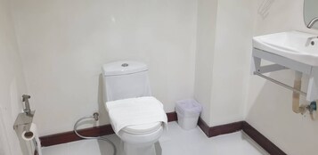 Un baño pequeño con inodoro, lavamanos y un cubo de basura.