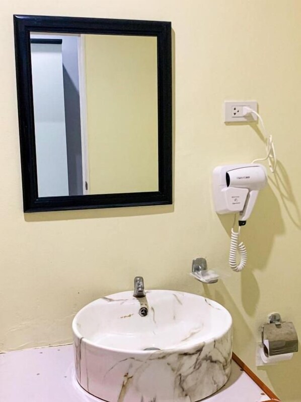 A bathroom with a marble sink, a mirror, a hairdryer, and a towel dispenser.