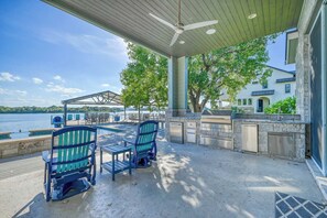 An outdoor patio with a view of the water, a covered seating area, and a stone fireplace. - The Bud Lane Collection | Infinity Pool, Dock & Waterslide (Kingsland)