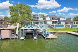 A waterfront property with a pool, a covered deck with chairs, and a small boat dock. - The Bud Lane Collection | Infinity Pool, Dock & Waterslide (Kingsland)