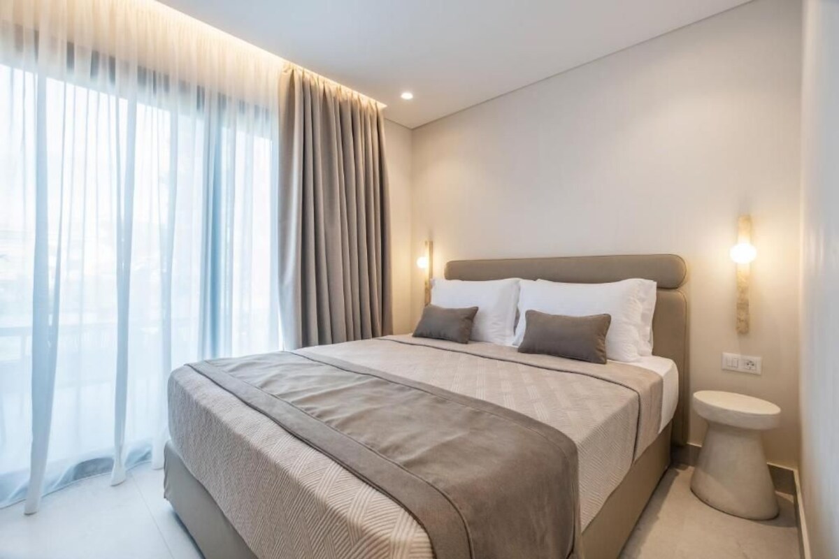 Una habitación de hotel moderna con una cama grande, una mesita de noche y vistas a través de cortinas traslúcidas.