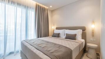 A modern hotel room with a large bed, a bedside table, and a view through sheer curtains.