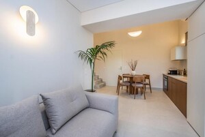 A modern living room with a sofa, a dining area with a table and chairs, and a kitchen area with cabinets and appliances.