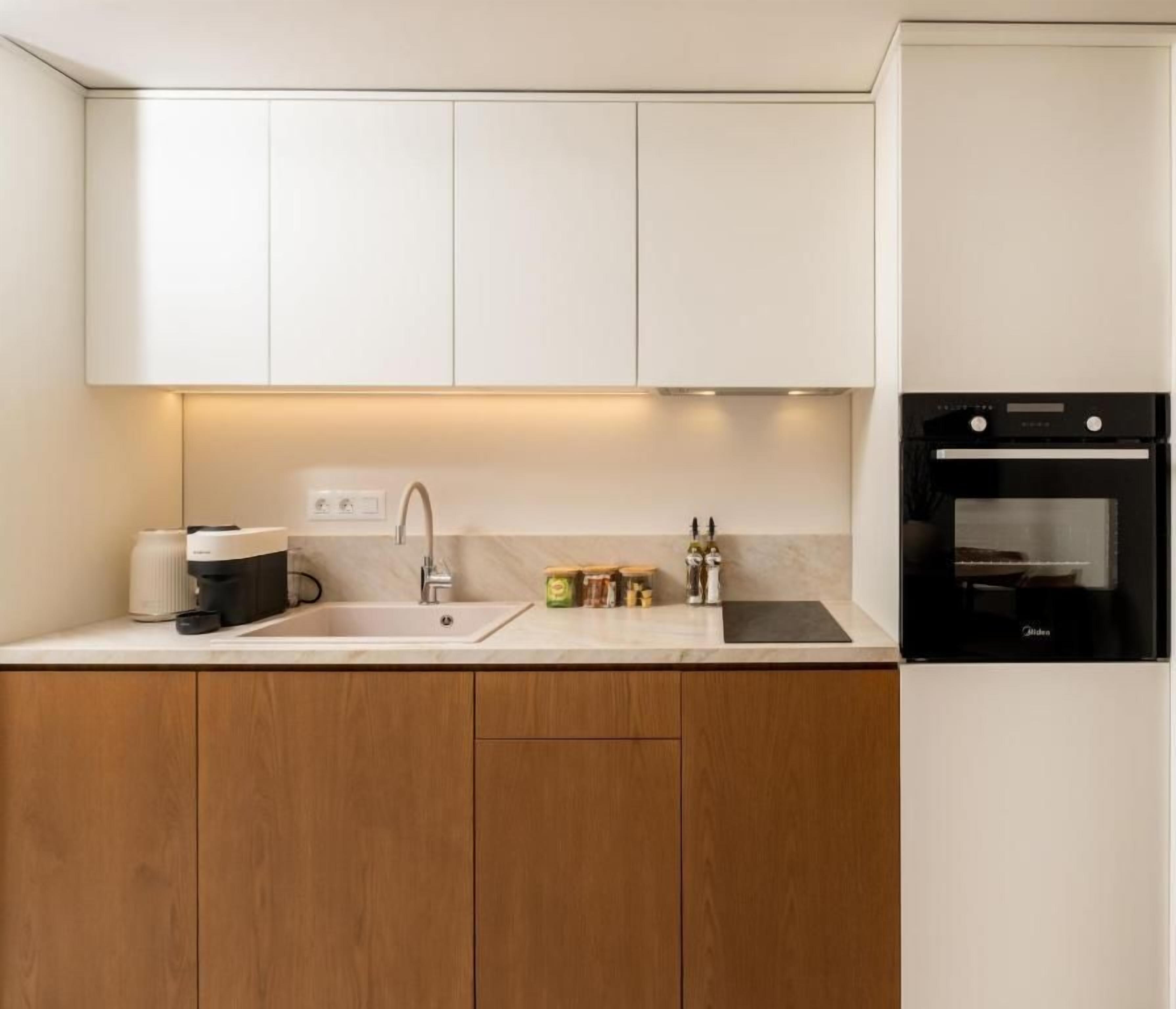 Una cocina moderna con armarios blancos, horno empotrado y una encimera con cafetera y frascos.