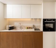A modern kitchen with white cabinets, a built-in oven, and a countertop with a coffee maker and jars.