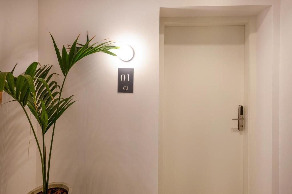 A door with a number plate, a potted plant, and a wall-mounted light fixture.