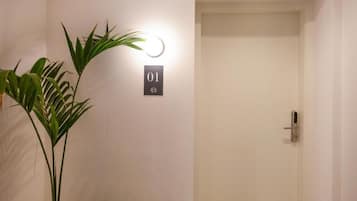A door with a number plate, a potted plant, and a wall-mounted light fixture.