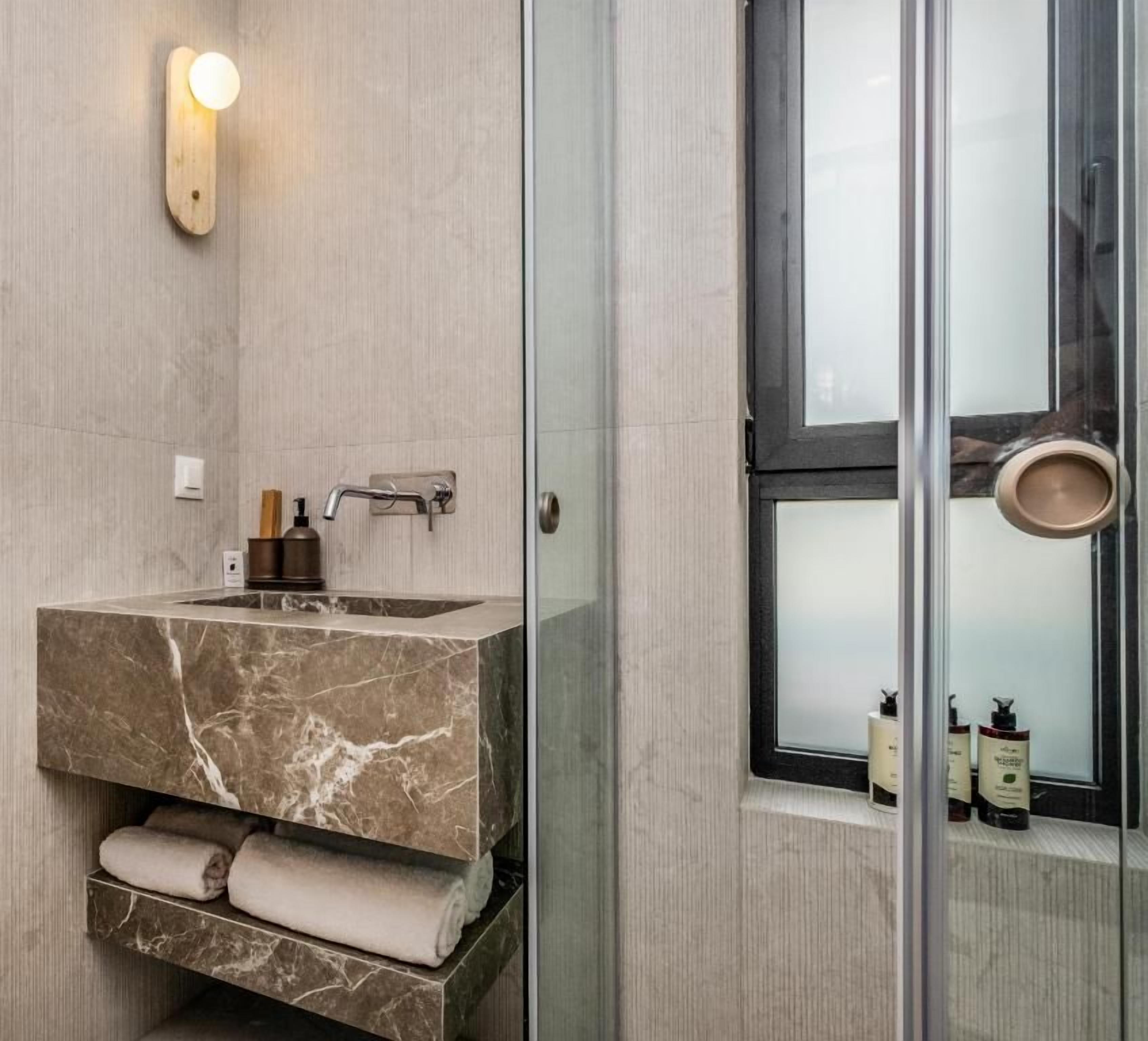 Baño con lavamanos de mármol, toallero y ventana con puerta de vidrio esmerilado.