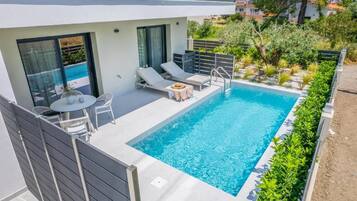 Ein moderner Poolbereich im Freien mit Liegestuhl, einem kleinen runden Tisch und einer Poolumrandung.