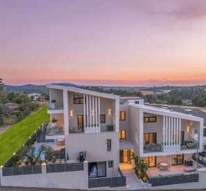 Um edifício moderno de dois andares com varandas, piscina e um jardim paisagístico.