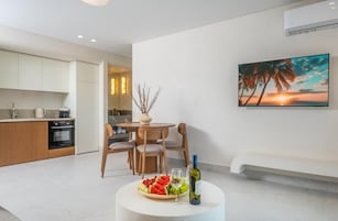 A modern kitchen with wooden cabinets, a dining area with a round table and chairs, a white bench, and a painting of a sunset.