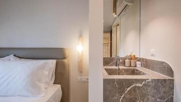 Une chambre d’hôtel moderne avec un lit, un meuble-lavabo en marbre et un grand miroir.