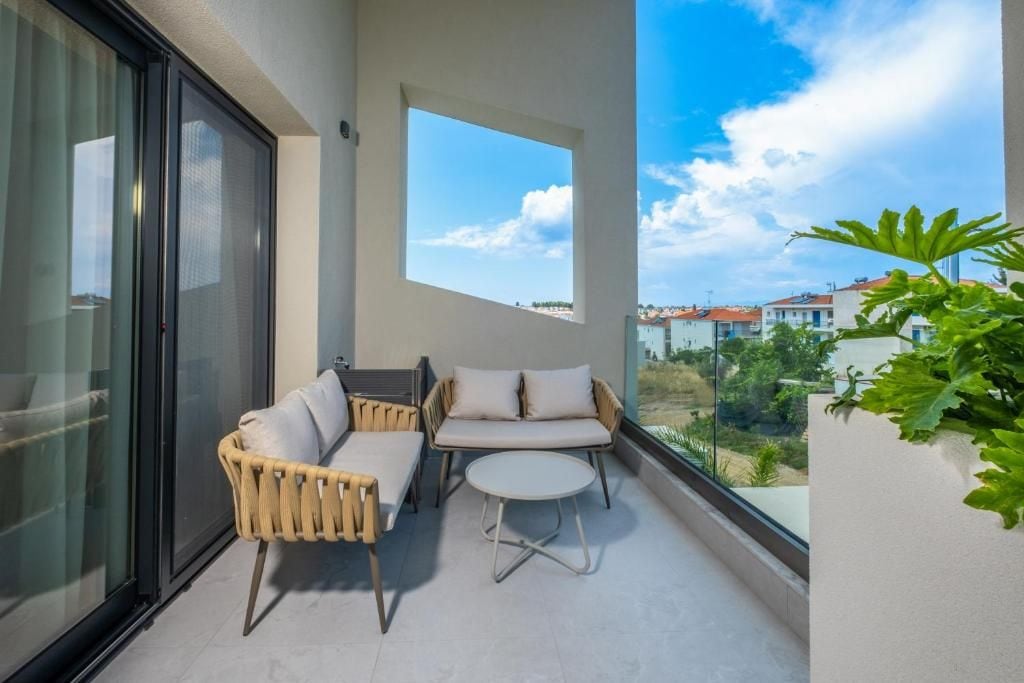 A balcony with a glass door, two wicker chairs, a small round table, and a potted plant.