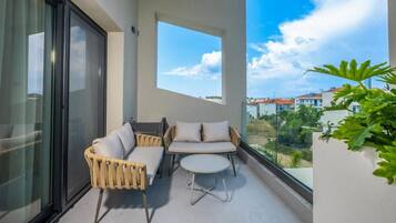 A balcony with a glass door, two wicker chairs, a small round table, and a potted plant.