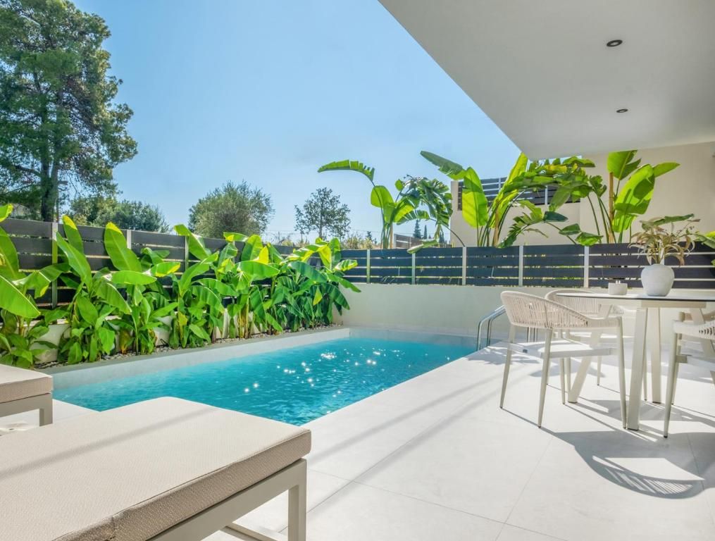 Ein moderner Poolbereich im Freien mit einem klaren, blauen Pool, umgeben von üppiger Bepflanzung und weißer Gartenmöbel.