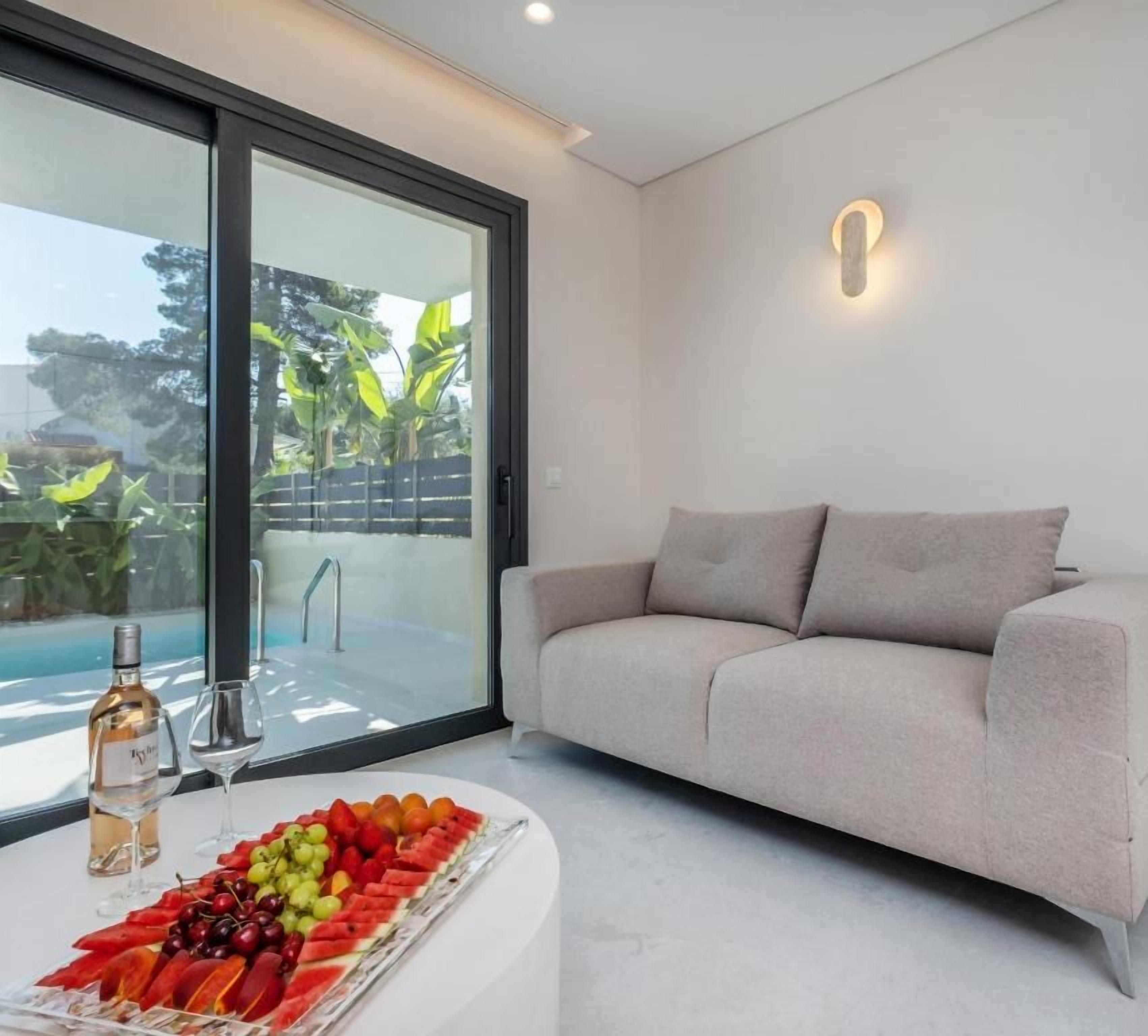 Una sala de estar moderna con un sofá, un ventanal que da a una piscina y un plato de frutas sobre una mesa.