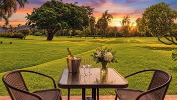 Een terras met een tafel, twee stoelen, een fles champagne en een bloevas.