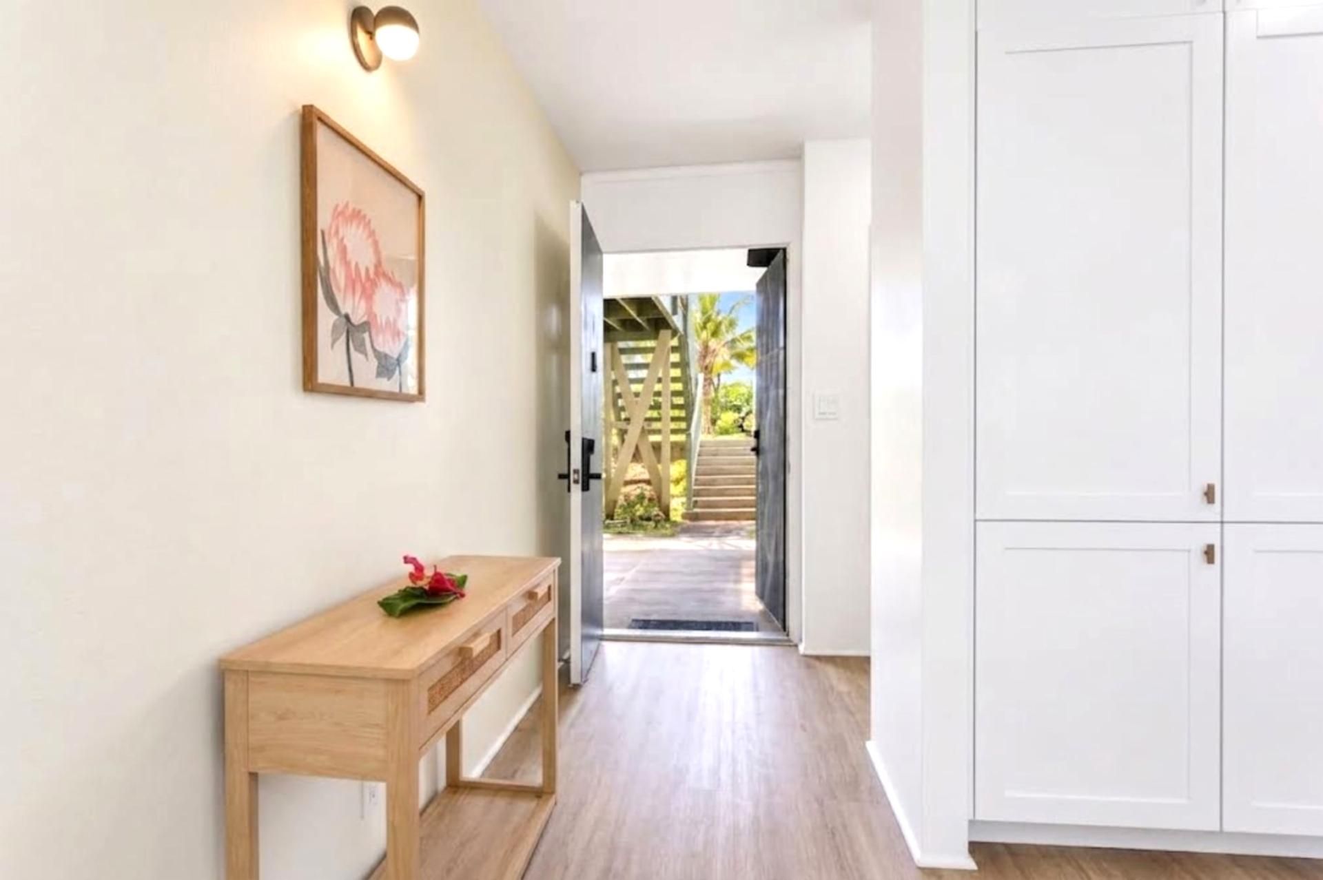 Un couloir avec un bureau en bois, un tableau encadré et une armoire blanche.