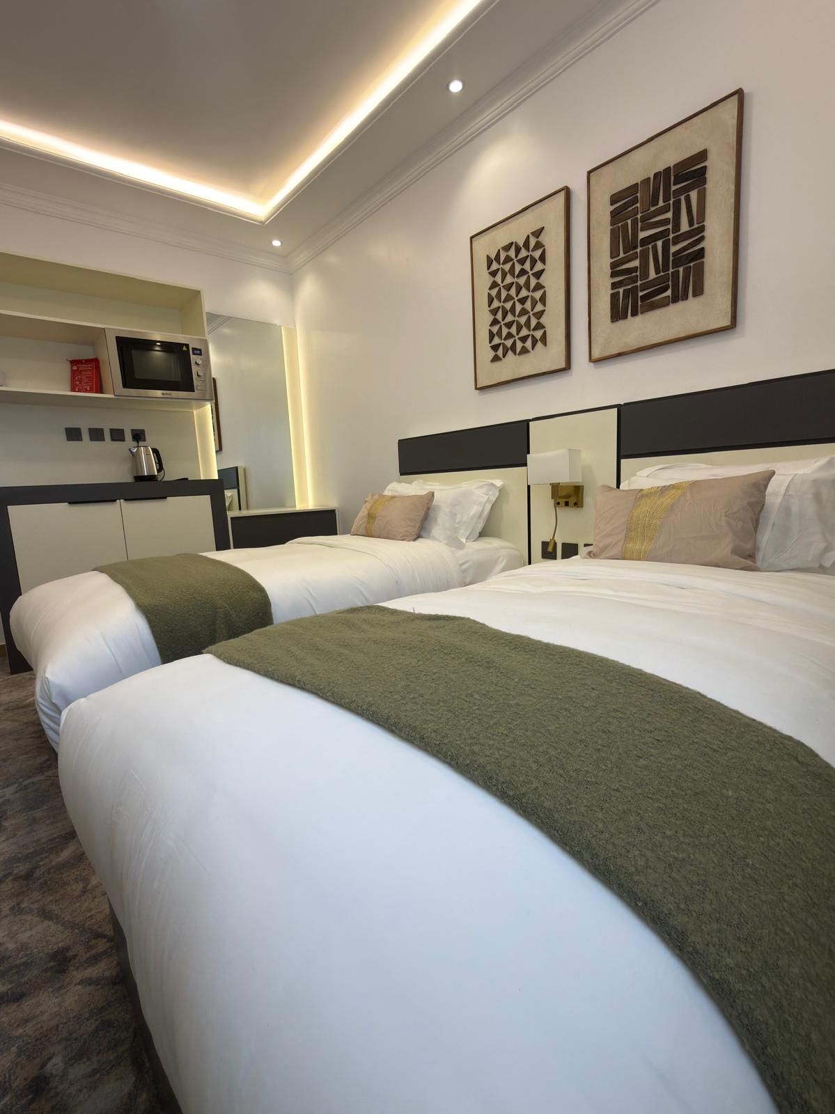 A hotel room with two beds, a kitchenette, and artwork on the walls.