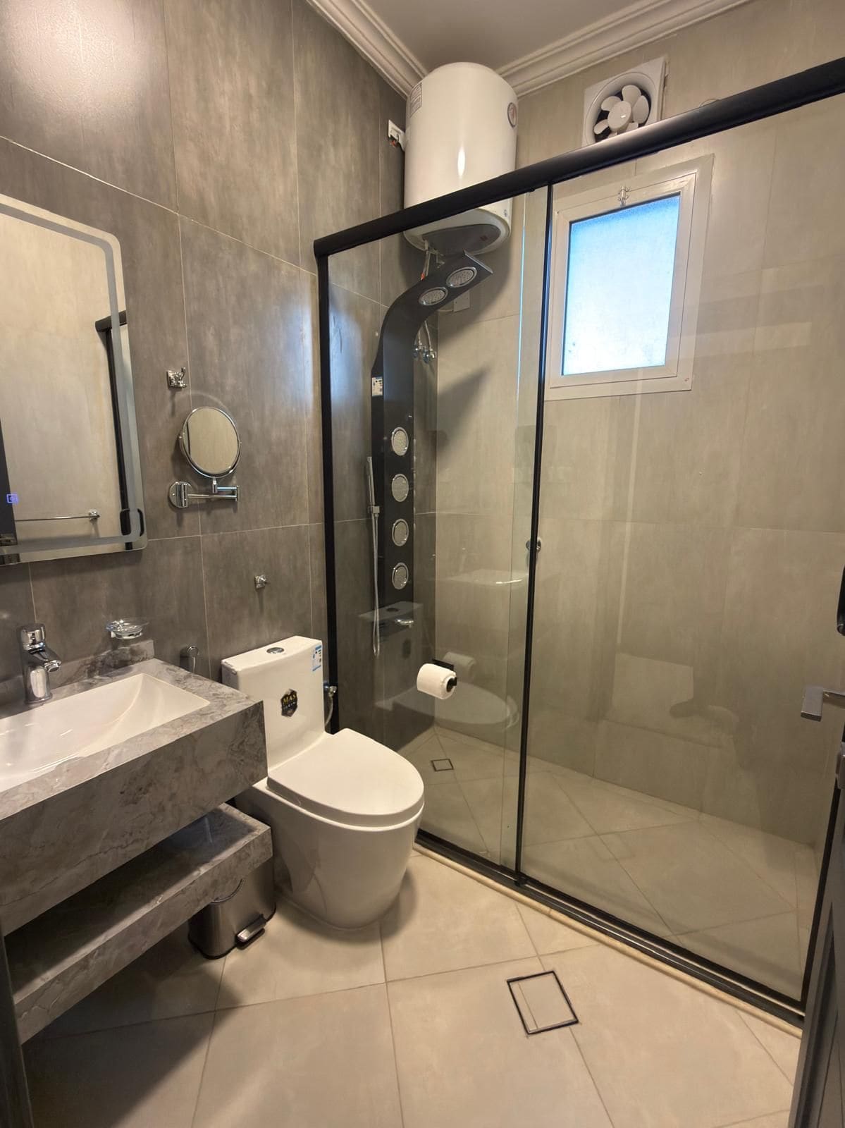 Ein modernes Badezimmer mit einer ein Glasfach umschlossenen Dusche, einer Toilette und einem Waschbecken mit Marmorplatte.